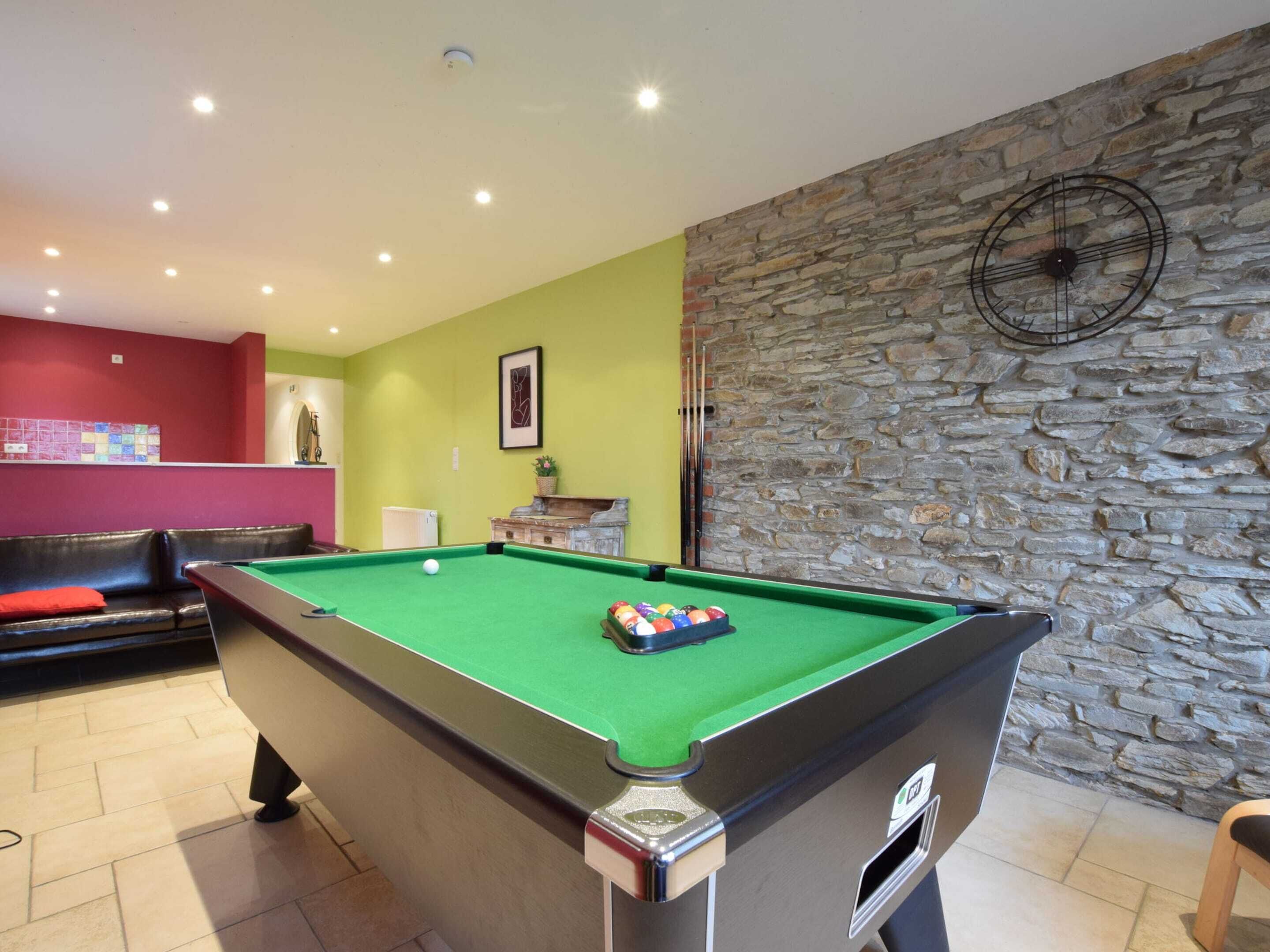 A pool table with a green felt surface, a stone wall, and a red couch in the background.