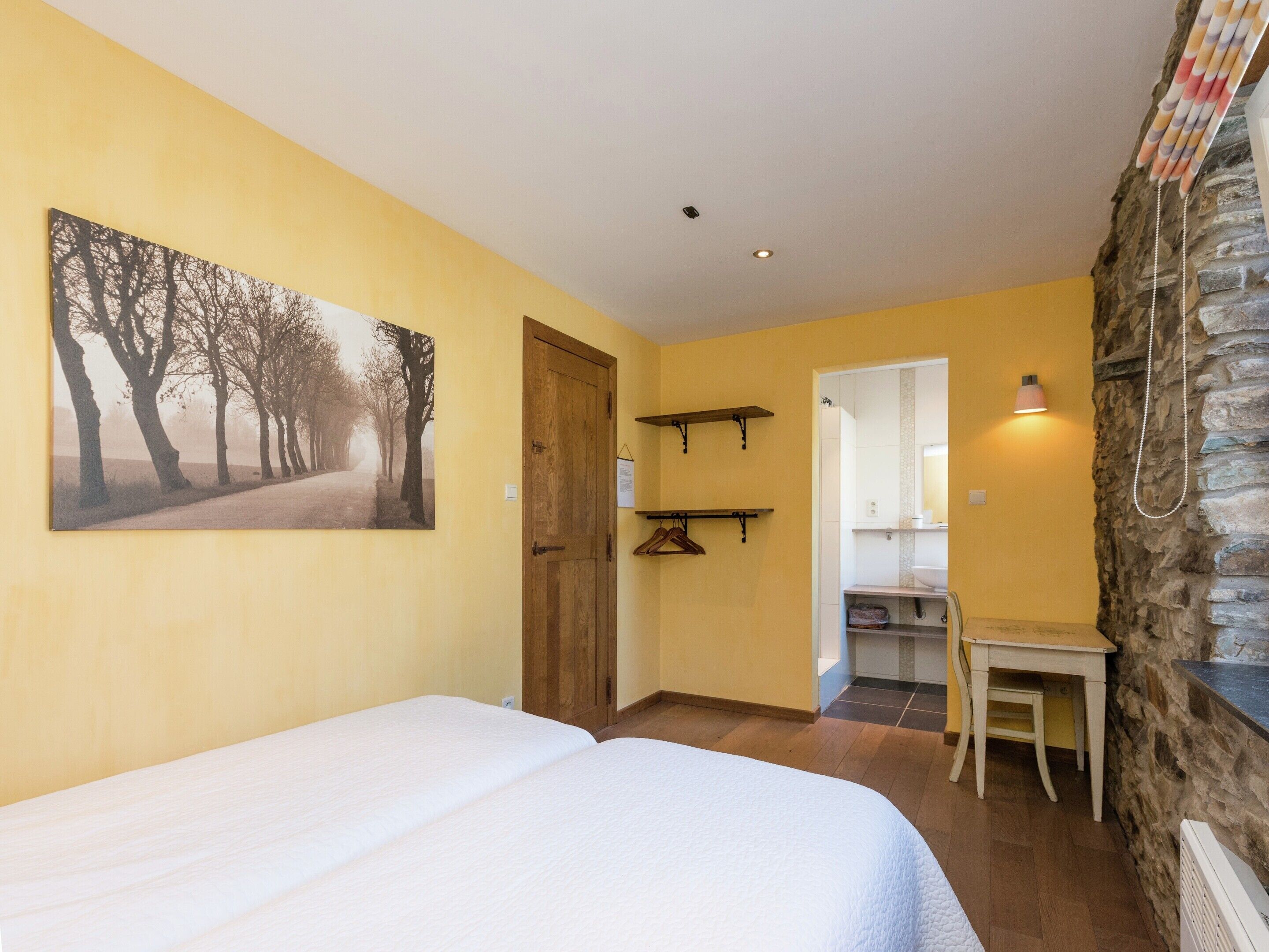 Un dormitorio con cama, puerta de madera, pasillo que conduce a un baño y pared de piedra.