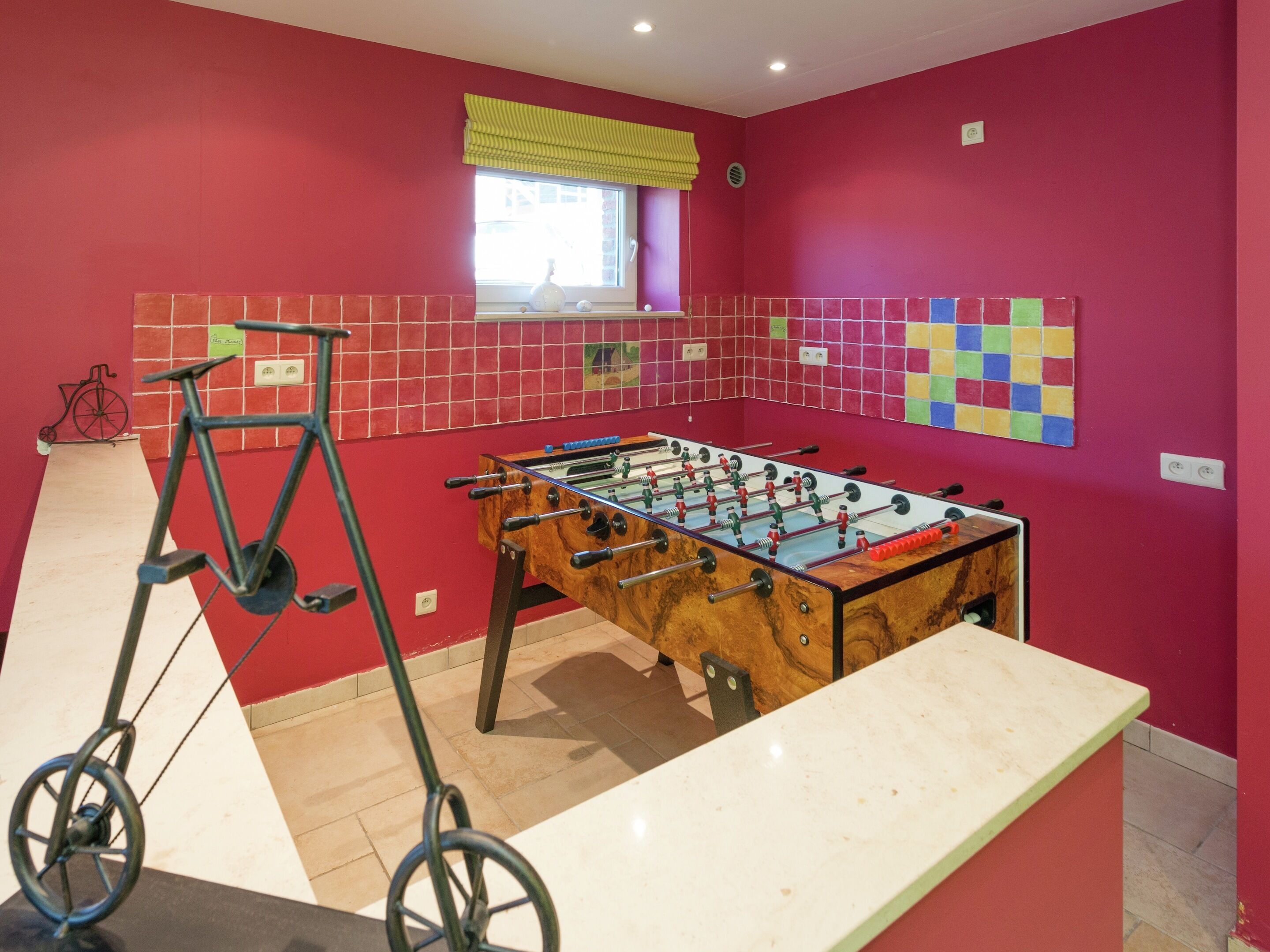Ein Zimmer mit Kicker, Fahrrad und einem Fenster mit gelbem Vorhang.