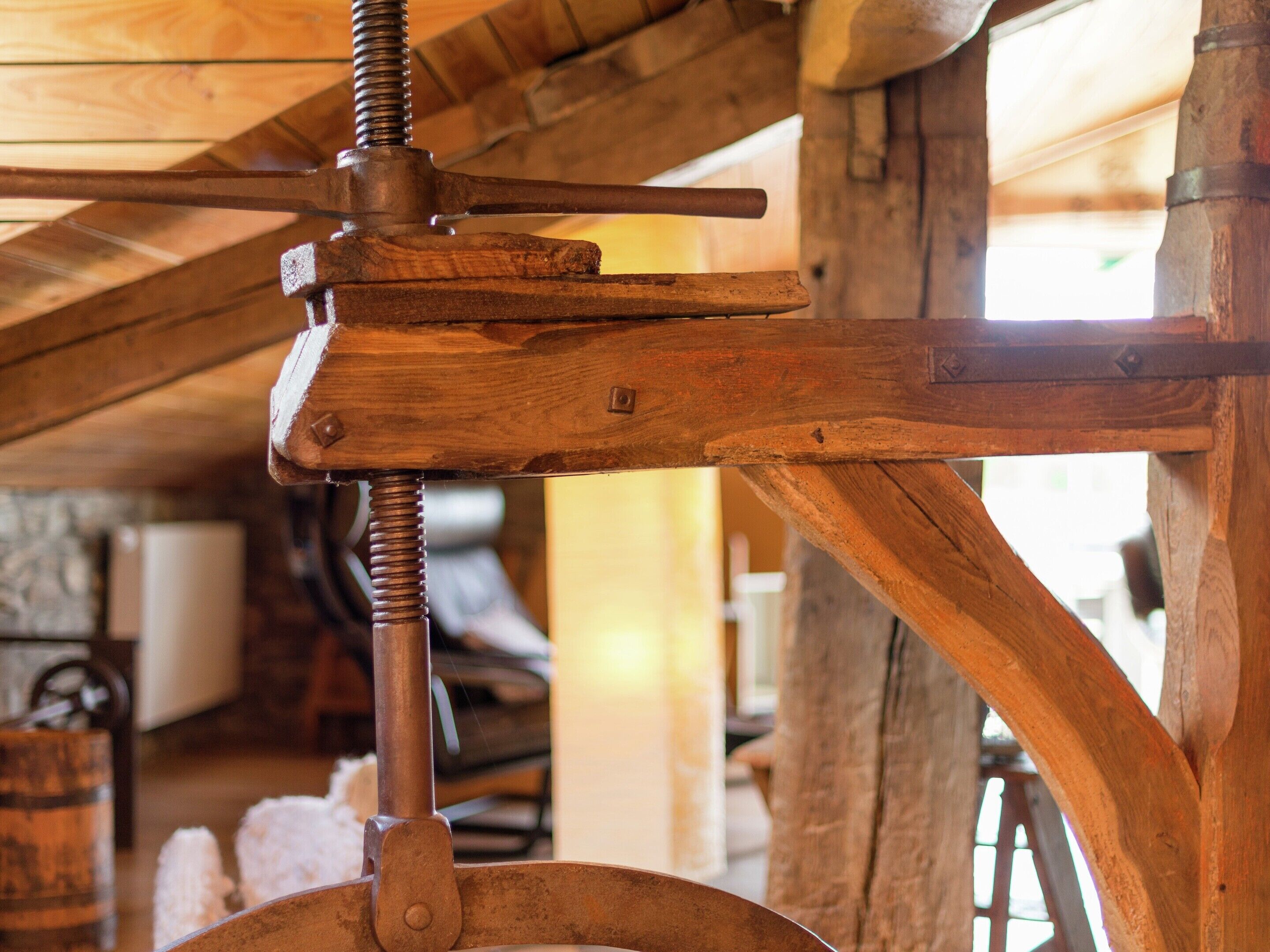 A wooden mechanical device, possibly a pulley system, in a rustic setting with wooden beams and a stone wall in the background.