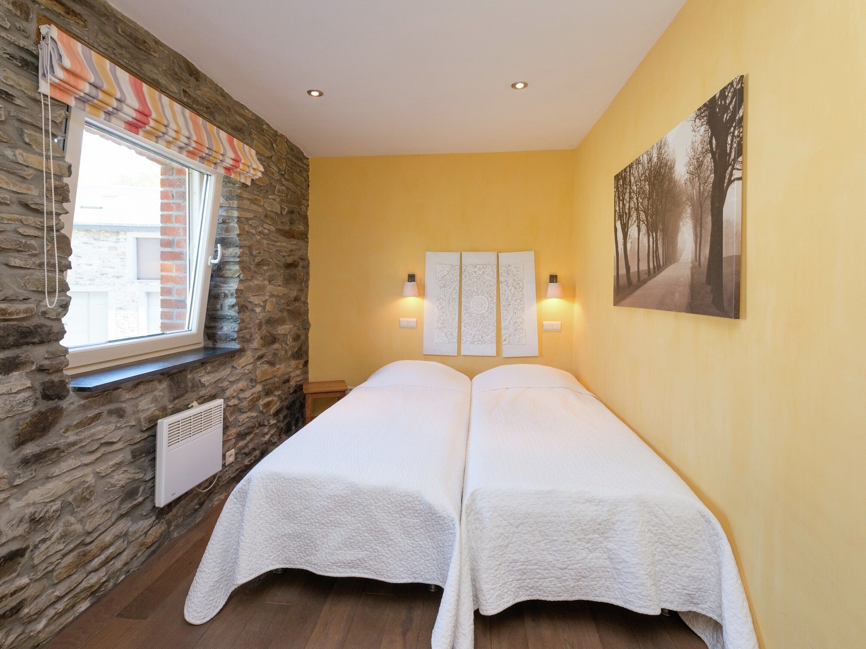 A room with two beds, a stone wall, a window with a striped blind, and a painting on the wall.