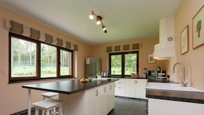 A modern kitchen with a central island, white cabinetry, and large windows offering a view of the outdoors. - Tenneville Villa With Sauna (Tenneville)