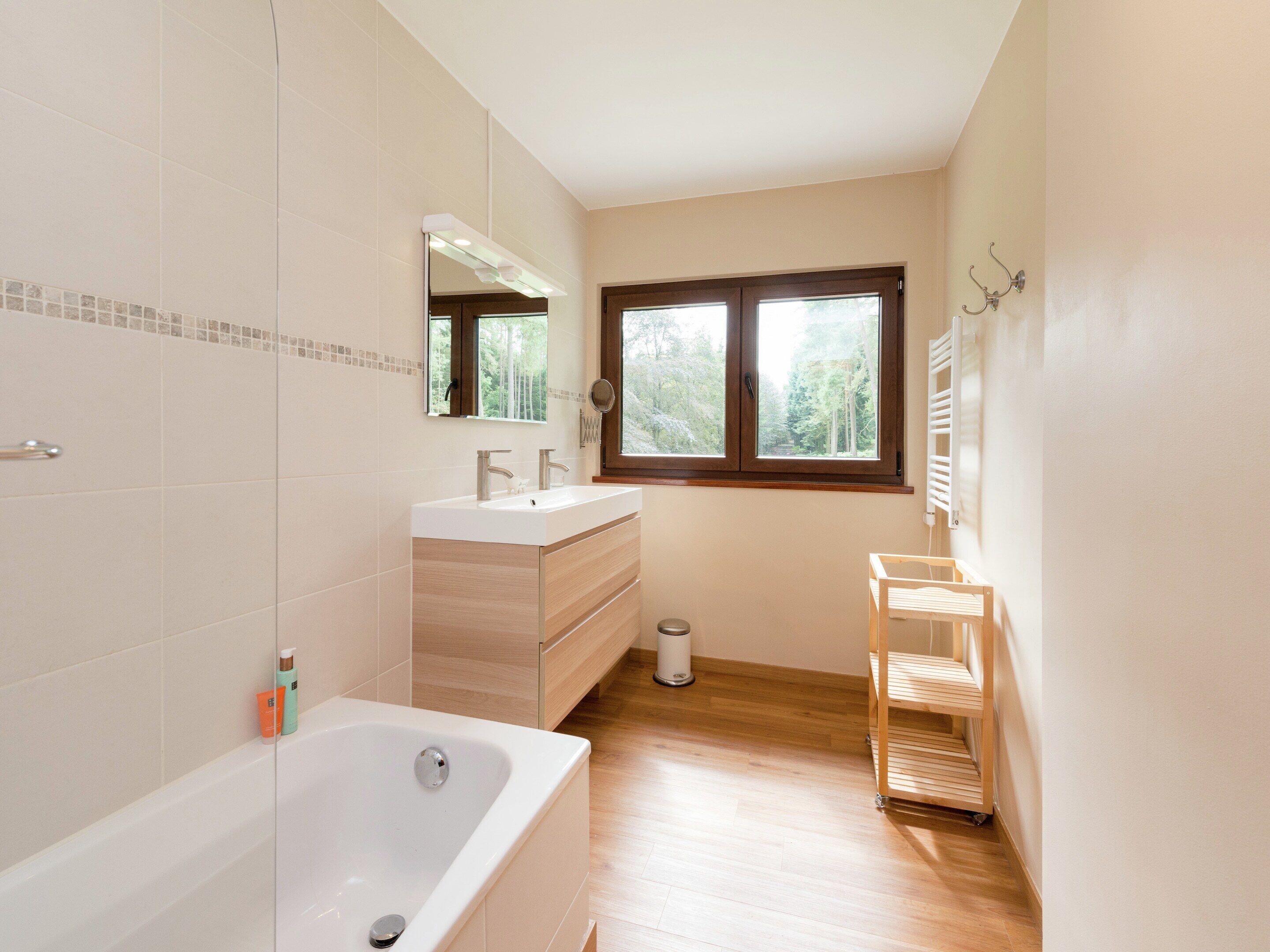 Une salle de bain moderne dotée d’une grande baignoire, d’un meuble-lavabo avec miroir et d’une fenêtre laissant entrer la lumière naturelle.