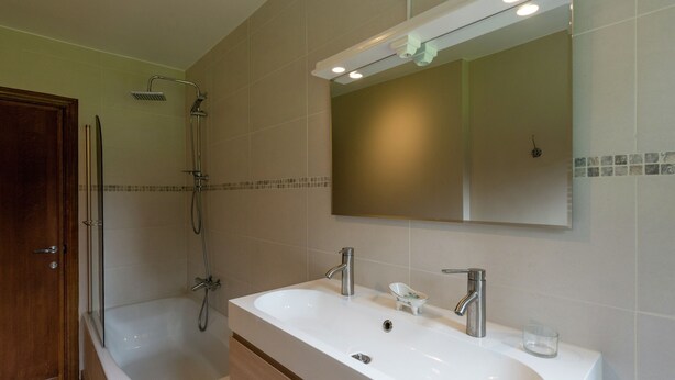 Ein Badezimmer mit einem Doppelwaschbecken, einer Dusche und einem Holzkabinet.