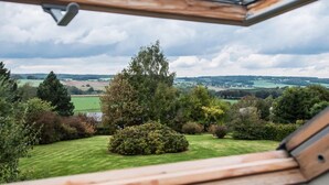Blick aus einem Fenster mit Holzrahmen auf eine grüne Landschaft mit Bäumen und Feldern.