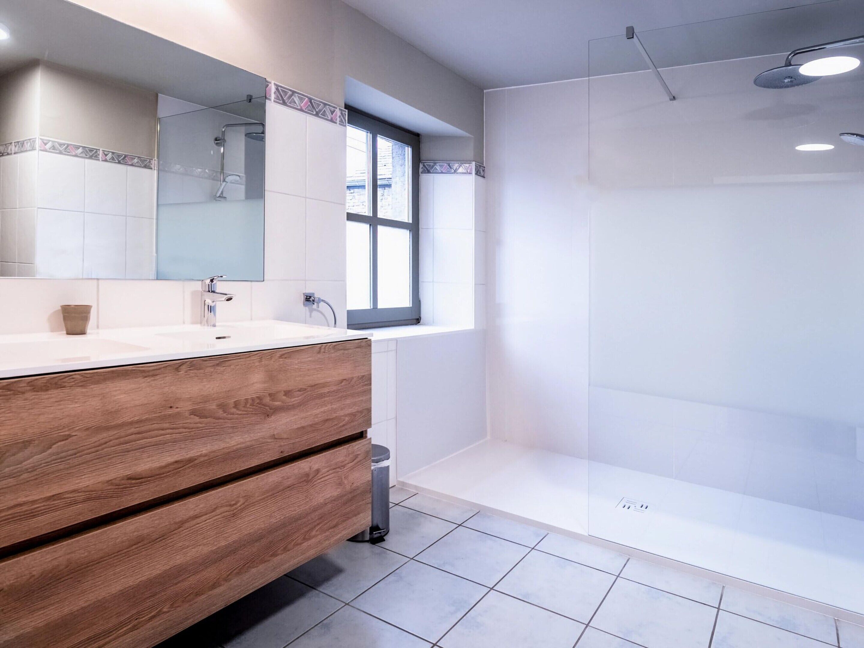 A modern bathroom with a wooden vanity, a large mirror, and a shower area.