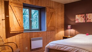 Ein Schlafzimmer mit Holzwänden, einem großen Fenster, einem Bett, einem Sessel, einem Heizkörper und einem Teppich.