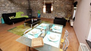 A dining area with a table set for four, a stone wall, and a black sofa. - Holiday Home in Limbourg With Garden (Limbourg)
