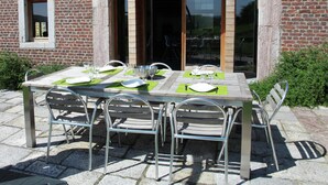 An outdoor dining area with a brick building, a large arched window, and a table set for four with metal chairs. - Holiday Home in Limbourg With Garden (Limbourg)