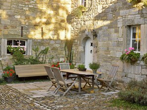 A stone building with a courtyard featuring a wooden table and chairs, a bench, and potted plants. - Limbourg Nature Retreat (Limbourg)
