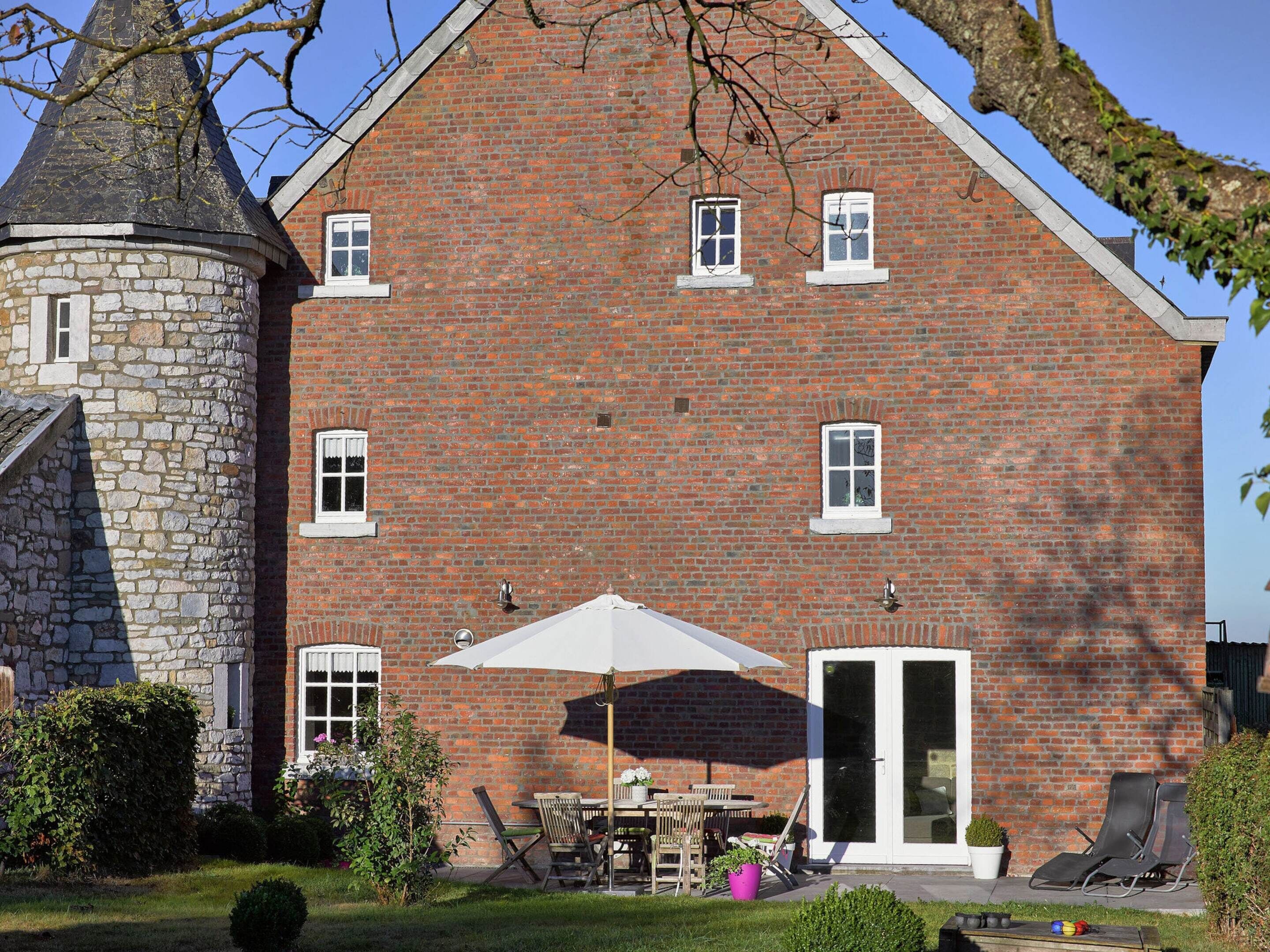 Un grand bâtiment en briques avec une tour en pierre, un patio avec des meubles d’extérieur et une porte-fenêtre coulissante.