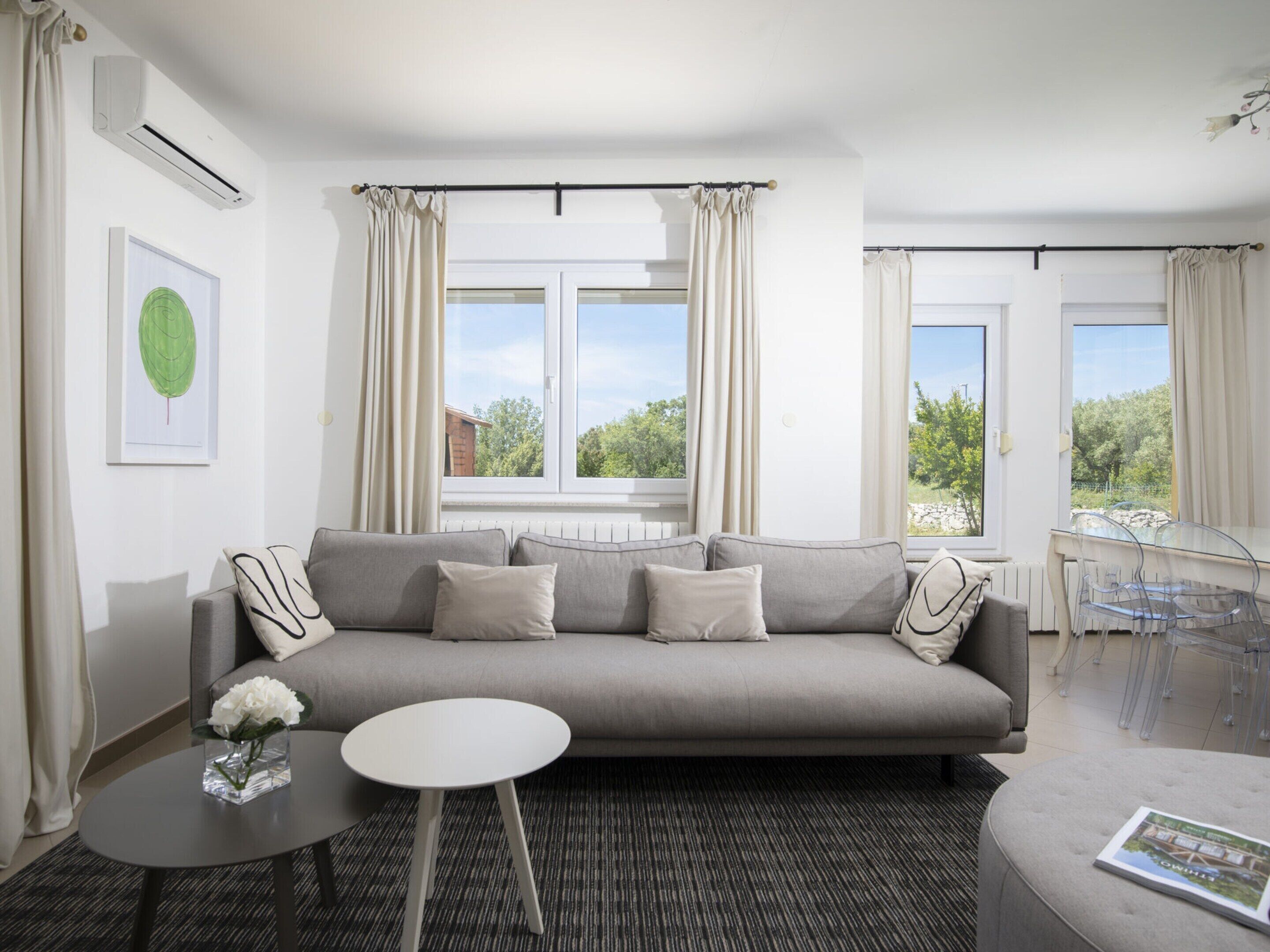 A modern living room with a grey sofa, a small round table, and a clear dining table.