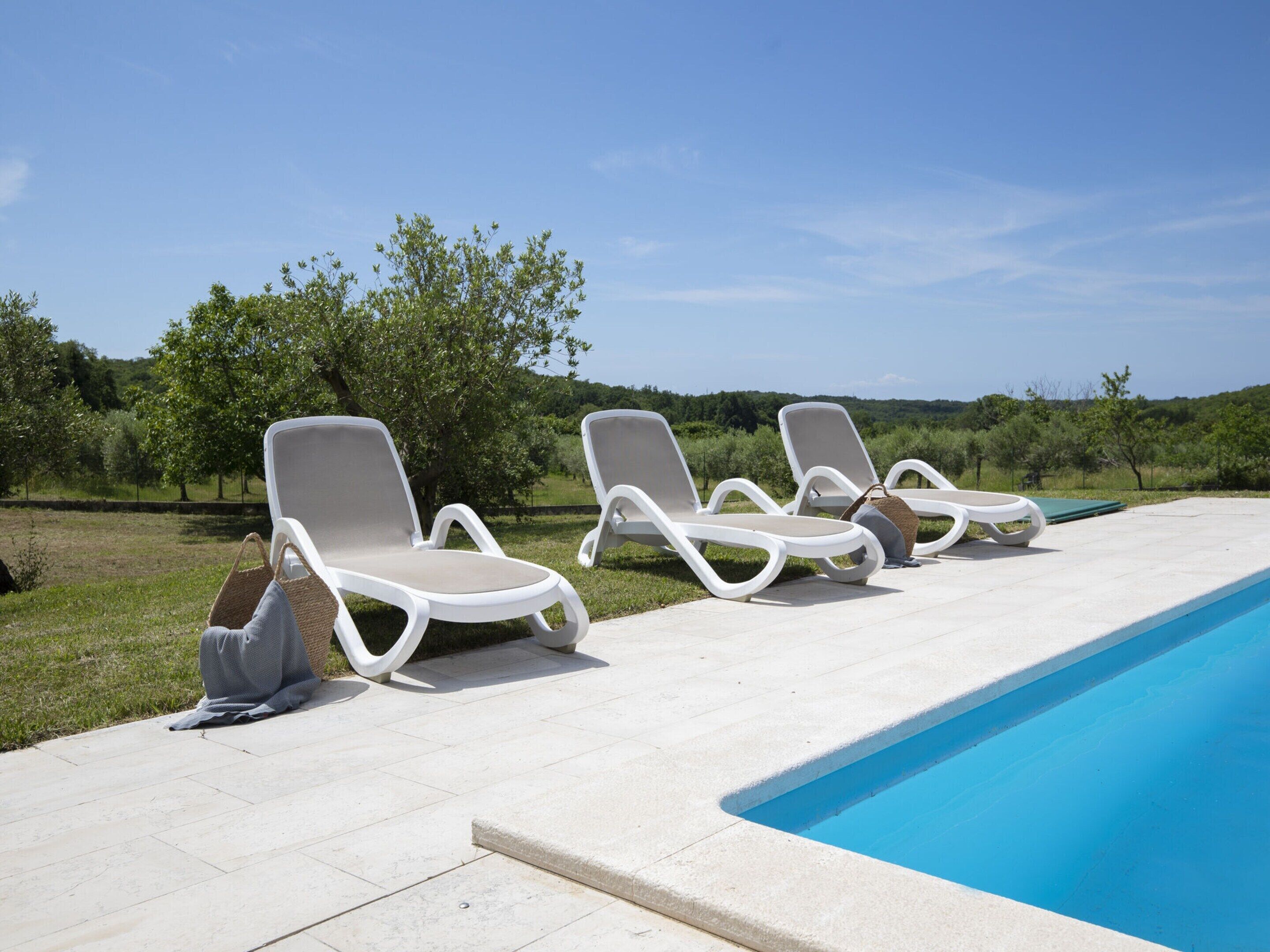 A poolside area with three white lounge chairs and a small bag on the ground.