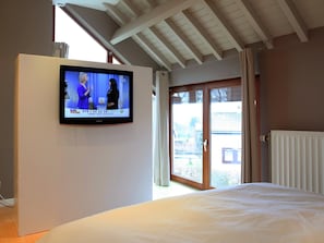 A bedroom with a bed, a television mounted on the wall, and a sliding glass door leading to an outdoor area. - Holiday Home in Waimes Near High Fens Reserve (Waimes)