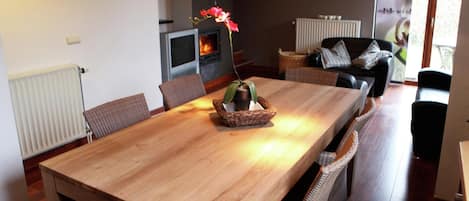A dining area with a wooden table, wicker chairs, a potted plant, and a fireplace.