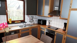 Ett kompakt kök med diskho, spis, mikrovågsugn och en matplats med bord och stolar.