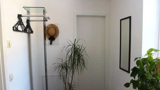 A hallway with a potted plant, a hat on the wall, and a coat rack with hangers. - Chicke Ferienwohnung in Struppen (Struppen)