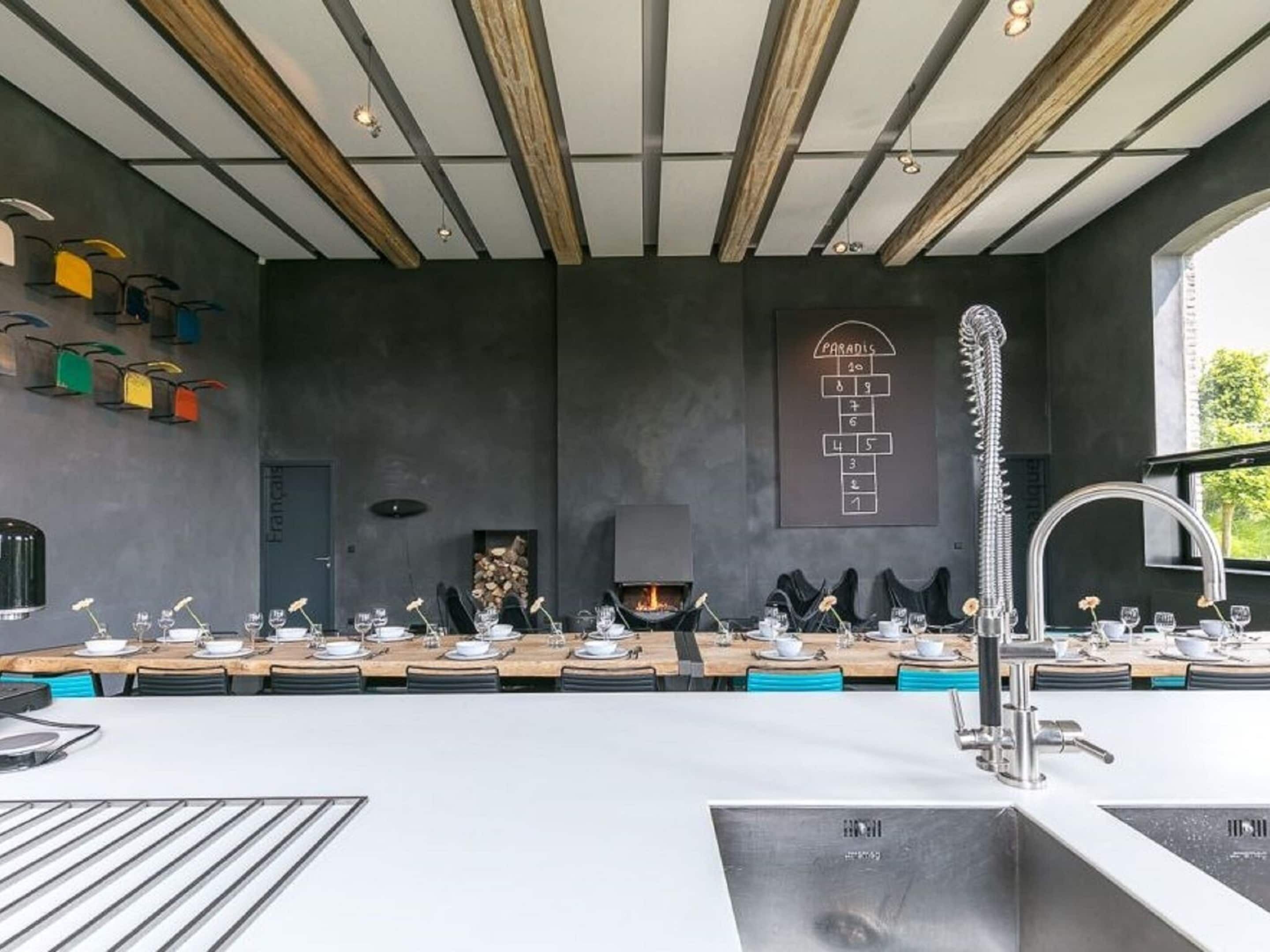 A modern kitchen with a long dining table, a built-in stove, and a large window.