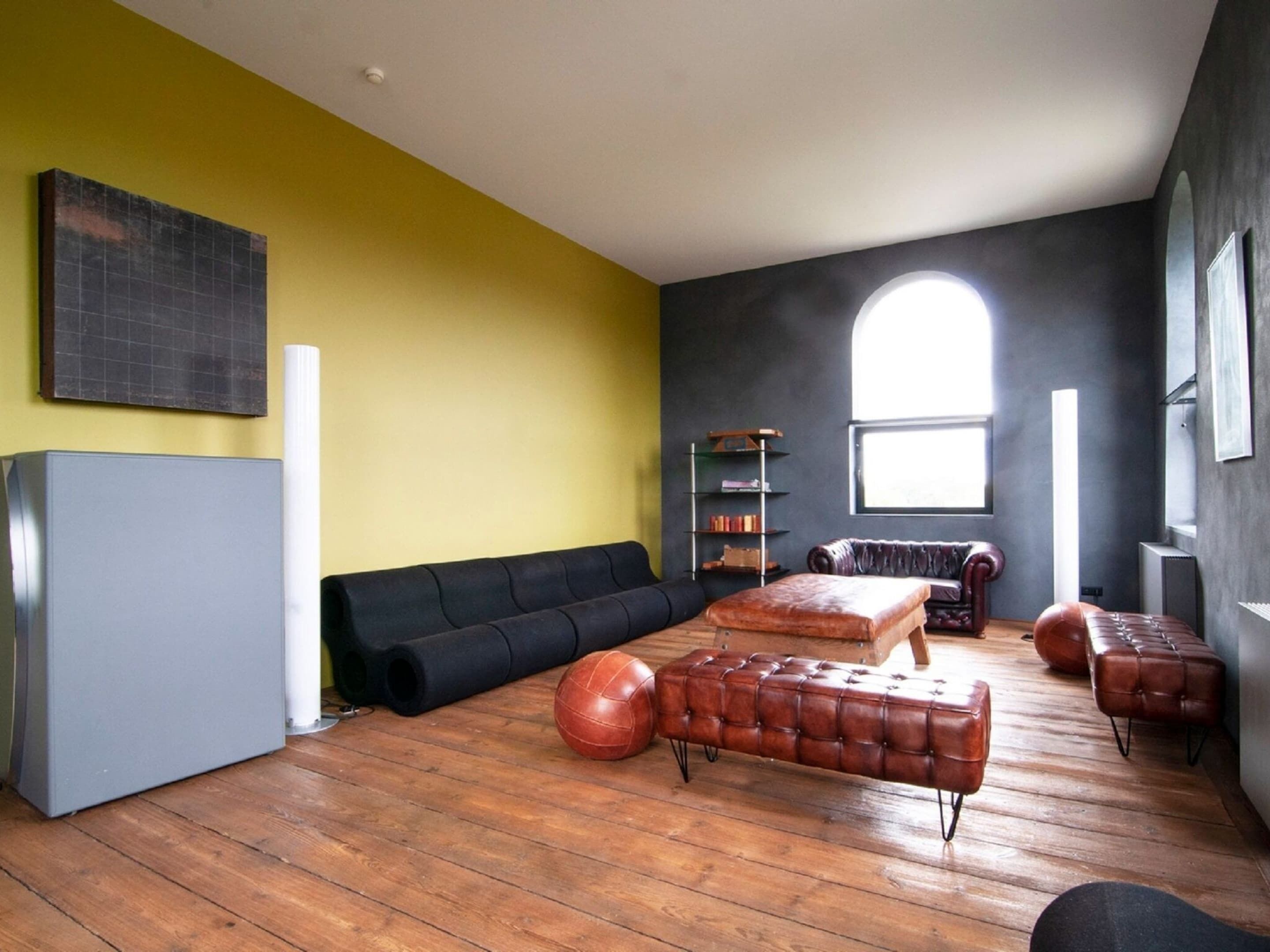 A modern living room with a black sofa, a brown leather ottoman, and a wooden coffee table.