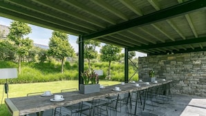 An outdoor dining area with a long table and chairs, surrounded by a stone wall and greenery. - Holiday Home in Denee for 21 People (Anhée)