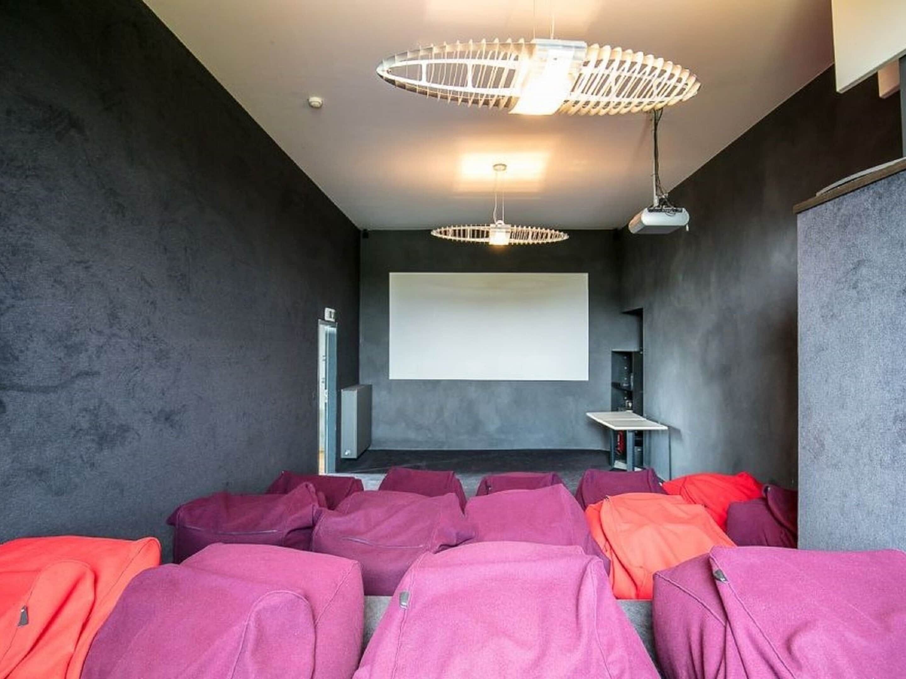 A modern room with a large screen, comfortable seating, and a unique ceiling light fixture.