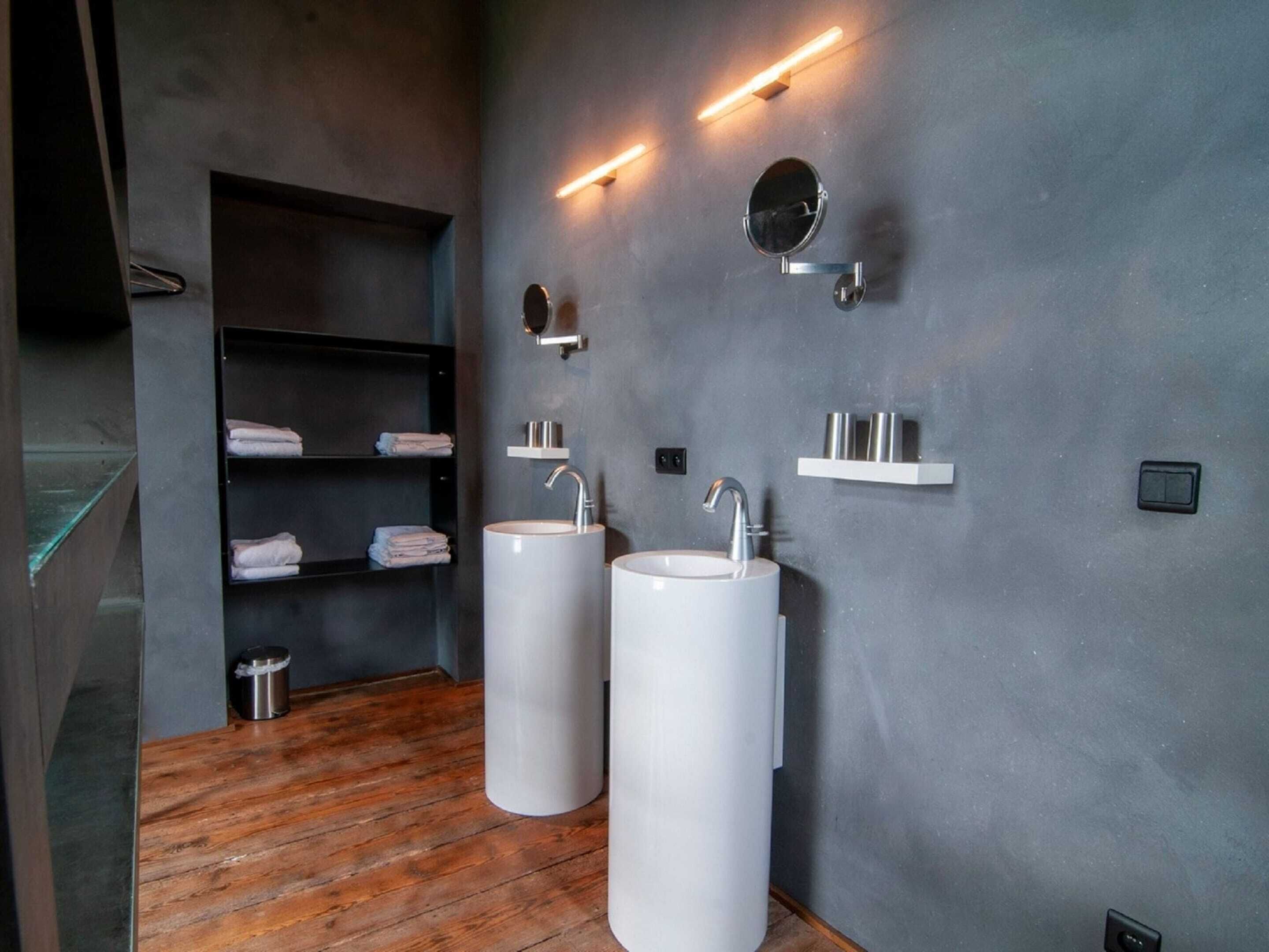 A modern bathroom with two large sinks, a wooden floor, and a dark gray wall with built-in shelves and lighting.