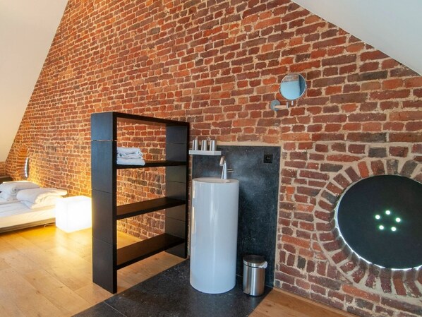 A modern bathroom with a brick wall, a black shelf with towels, a white sink, and a circular mirror.