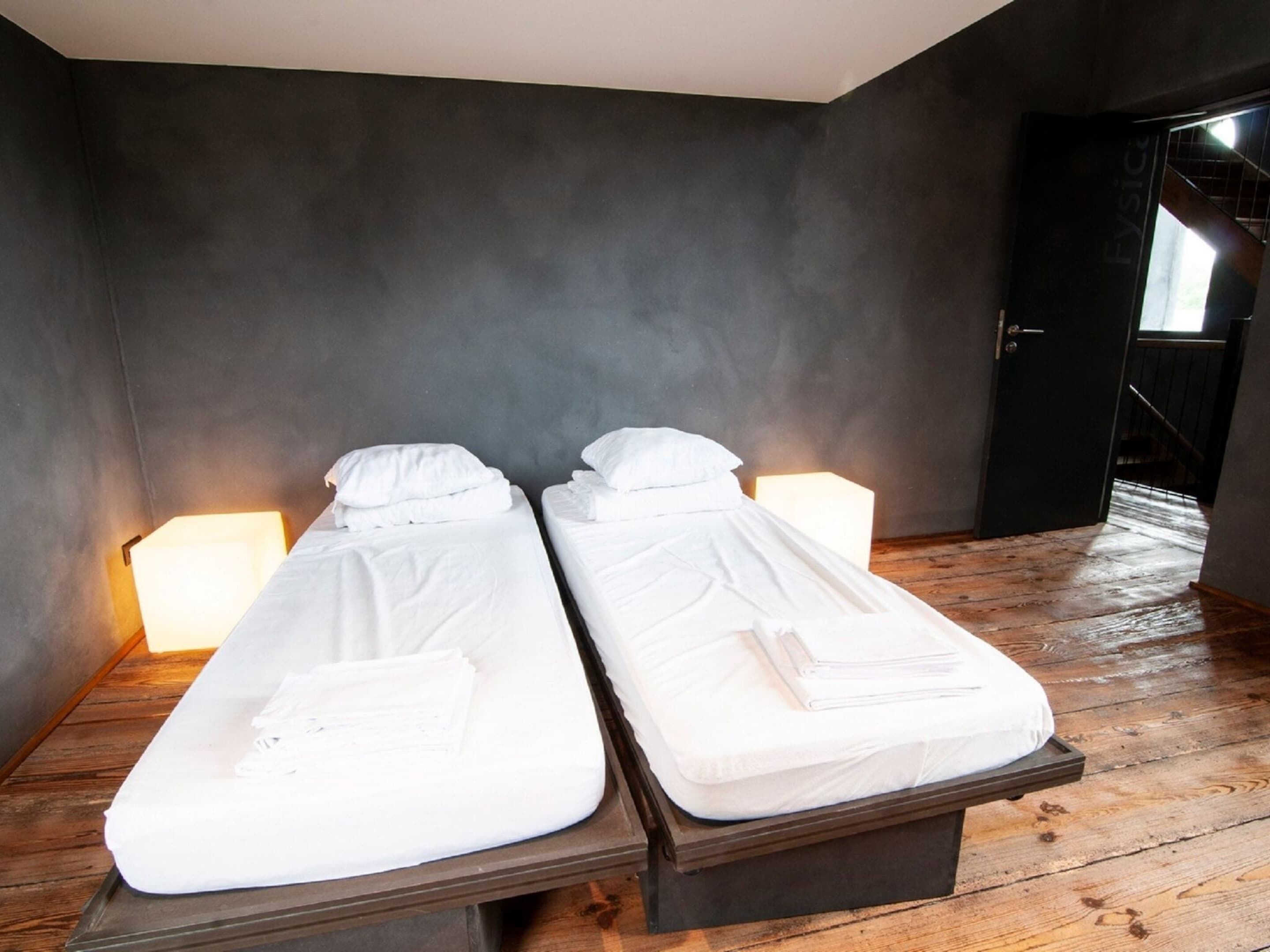 Two massage tables with white linens in a room with dark walls and wooden flooring.