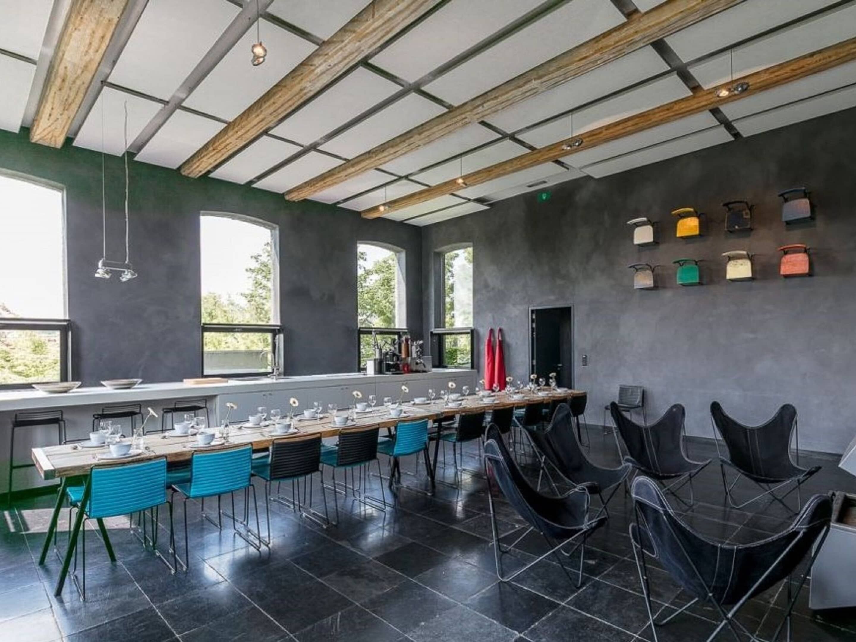 A modern dining area with a long table set for a meal, surrounded by chairs, and large windows providing natural light.