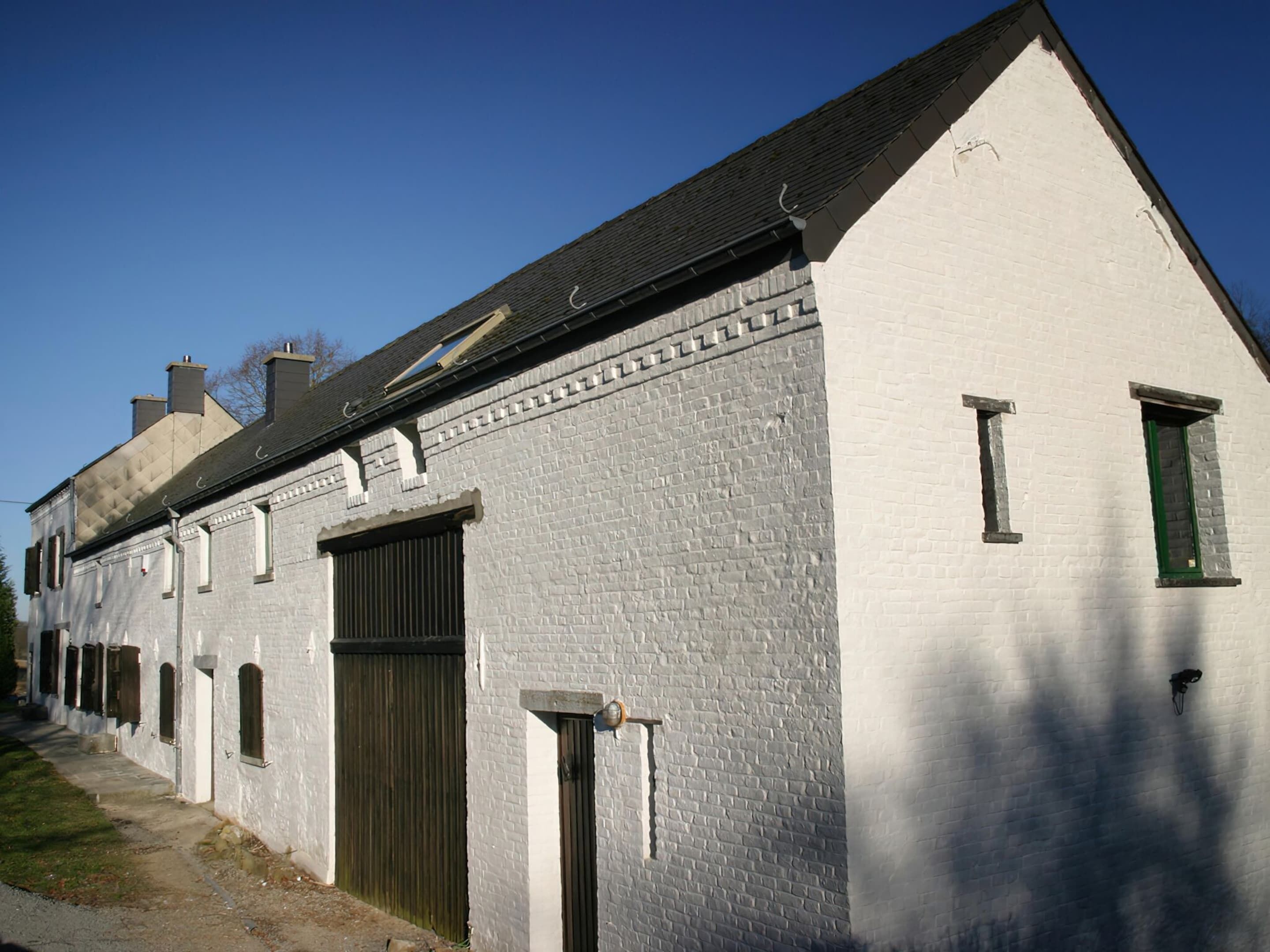 Um edifício de tijolos brancos com telhado empena e várias janelas, além de uma porta grande.