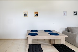 Un salon minimaliste avec une table en bois, un canapé gris et trois œuvres d’art encadrées accrochées au mur.