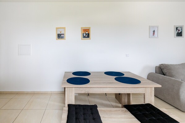 A minimalist living room with a wooden table, a grey sofa, and three framed artworks on the wall.
