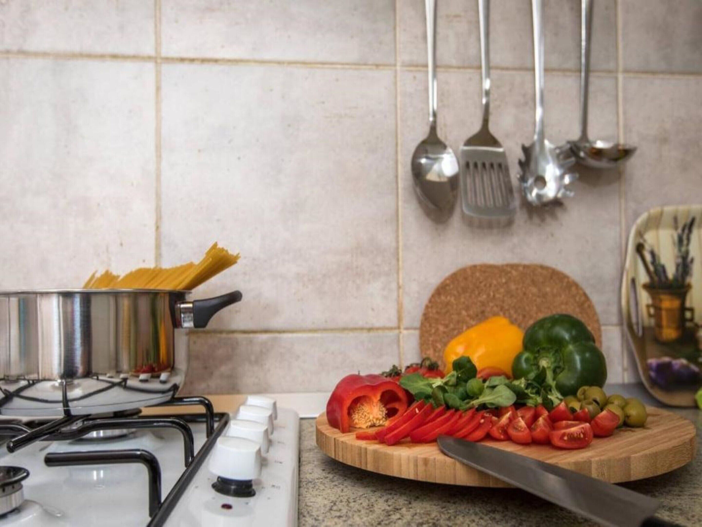 A kitchen with a gas stove, a cutting board with vegetables, and hanging utensils.