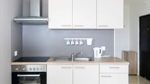 Een moderne keuken met witte kasten, een roestvrijstalen oven, een gasfornuis, een spoelbak en een waterkoker.