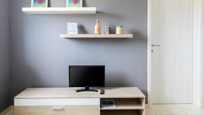 Een moderne kamer met een televisie op een houten bureau, twee wandplanken met decoratieve objecten en een deur.