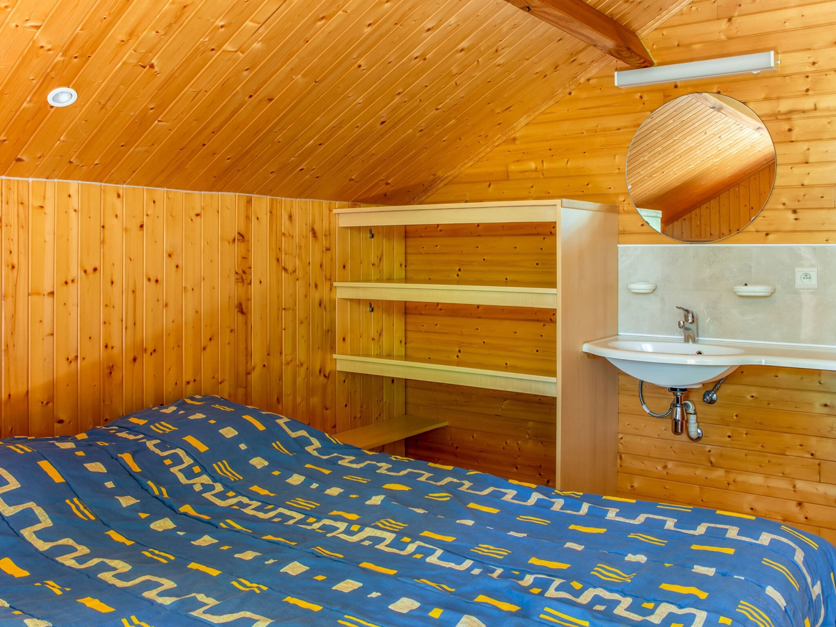 Een kamer met houten lambrisering, een bed, een inbouwplank en een wastafel aan de muur.