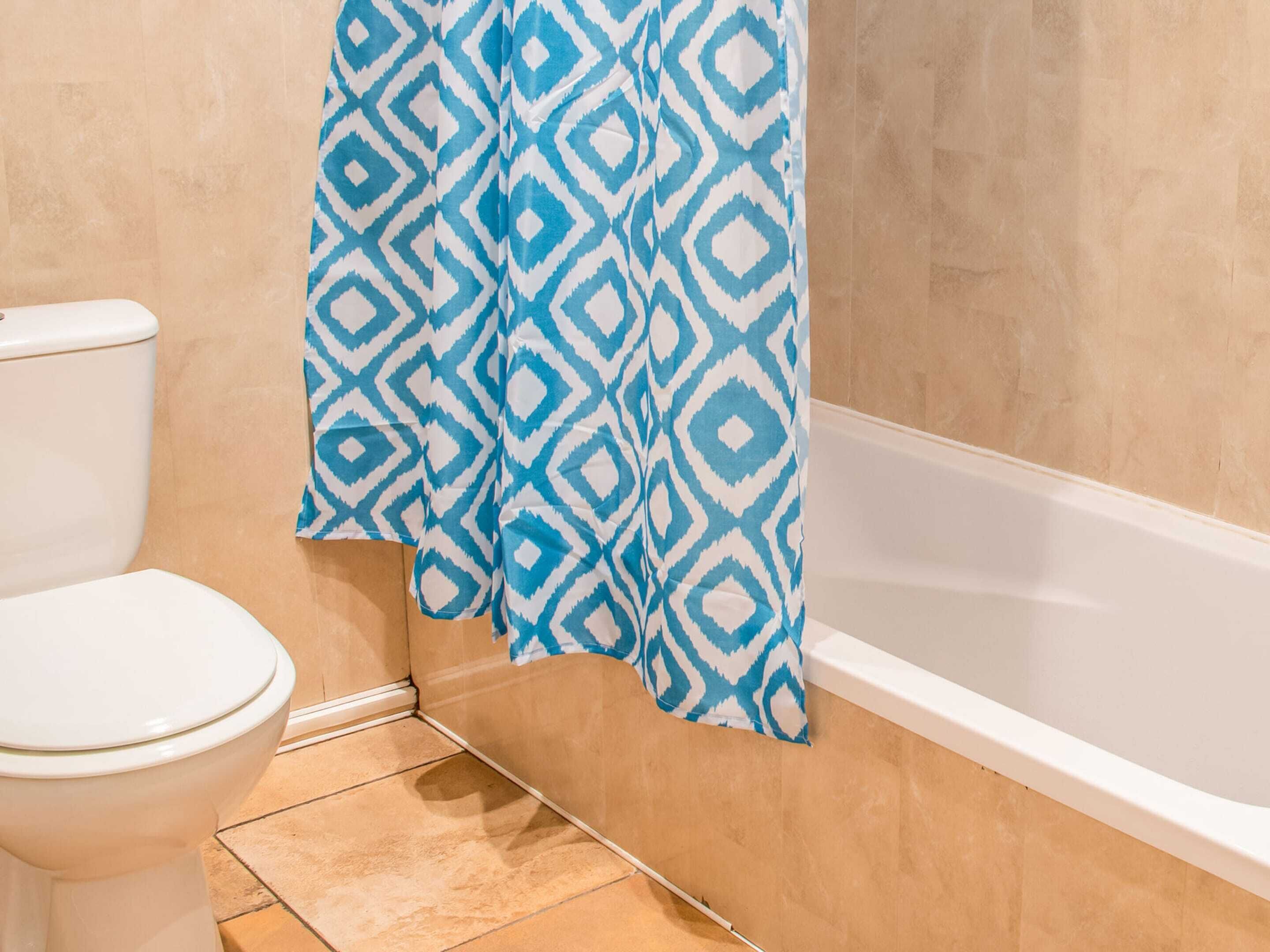 Un bagno con il water, una vasca e una tenda da doccia con motivo geometrico.