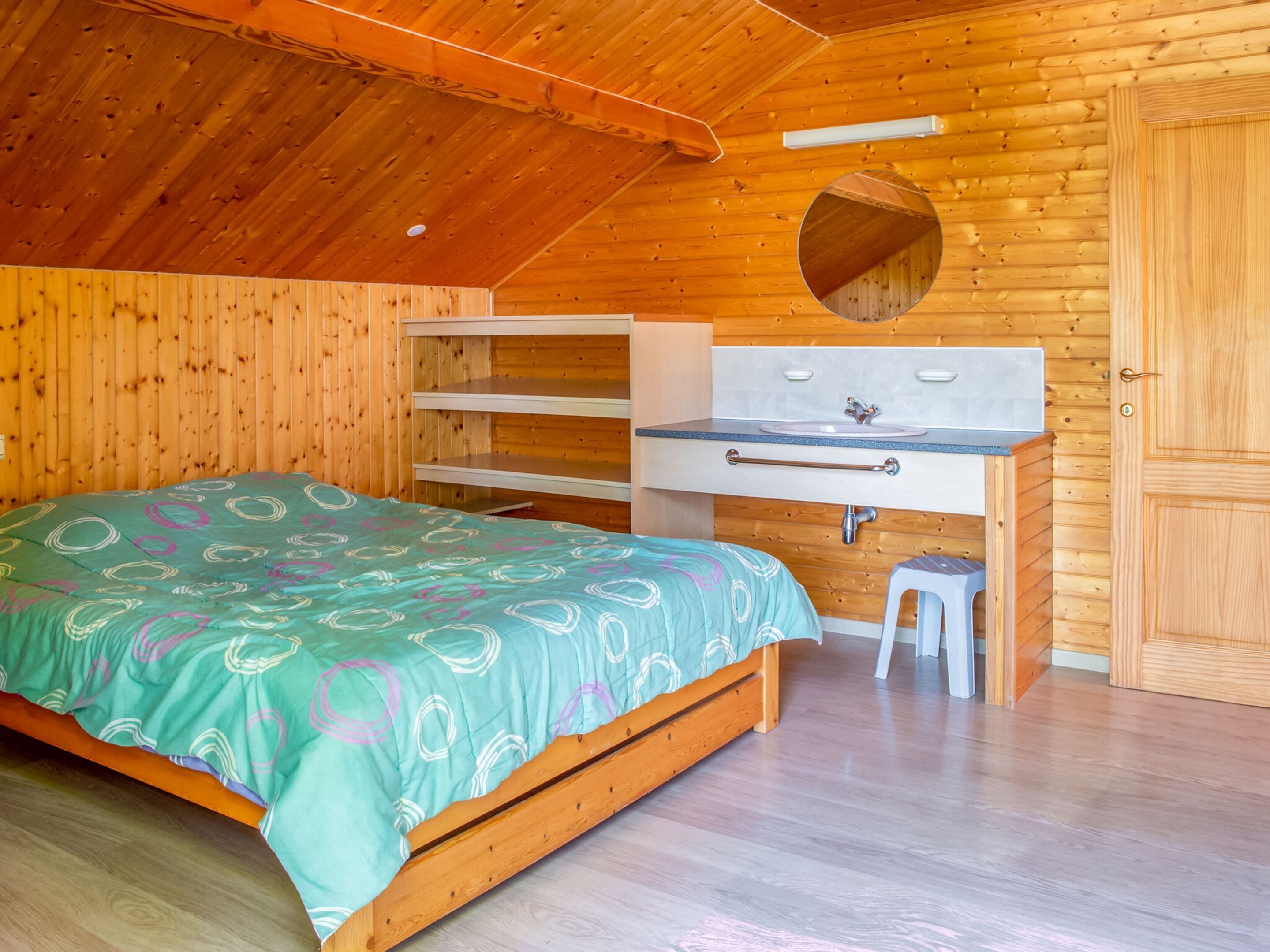 A cozy wooden cabin bedroom with a bed, a desk, and a mirror.