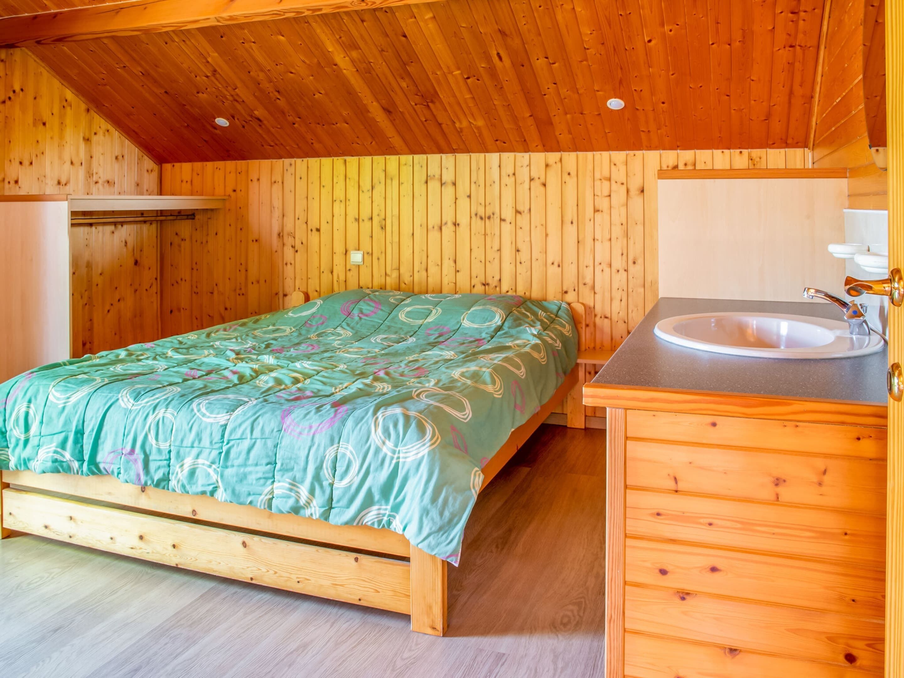 Ein Schlafzimmer einer Holzhütte mit einem Bett, einer Holzkommode und einem Waschbecken.