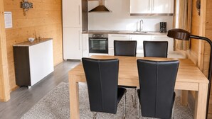 Une cuisine compacte avec des meubles blancs, une cuisinière et un évier. On y trouve une table à manger avec quatre chaises.