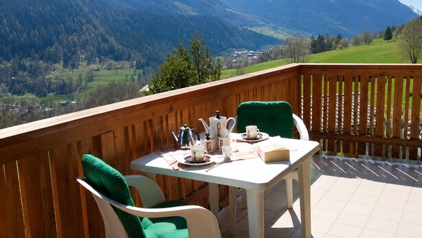 Un balcon avec une table dressée pour deux personnes, offrant une vue sur un paysage montagneux.