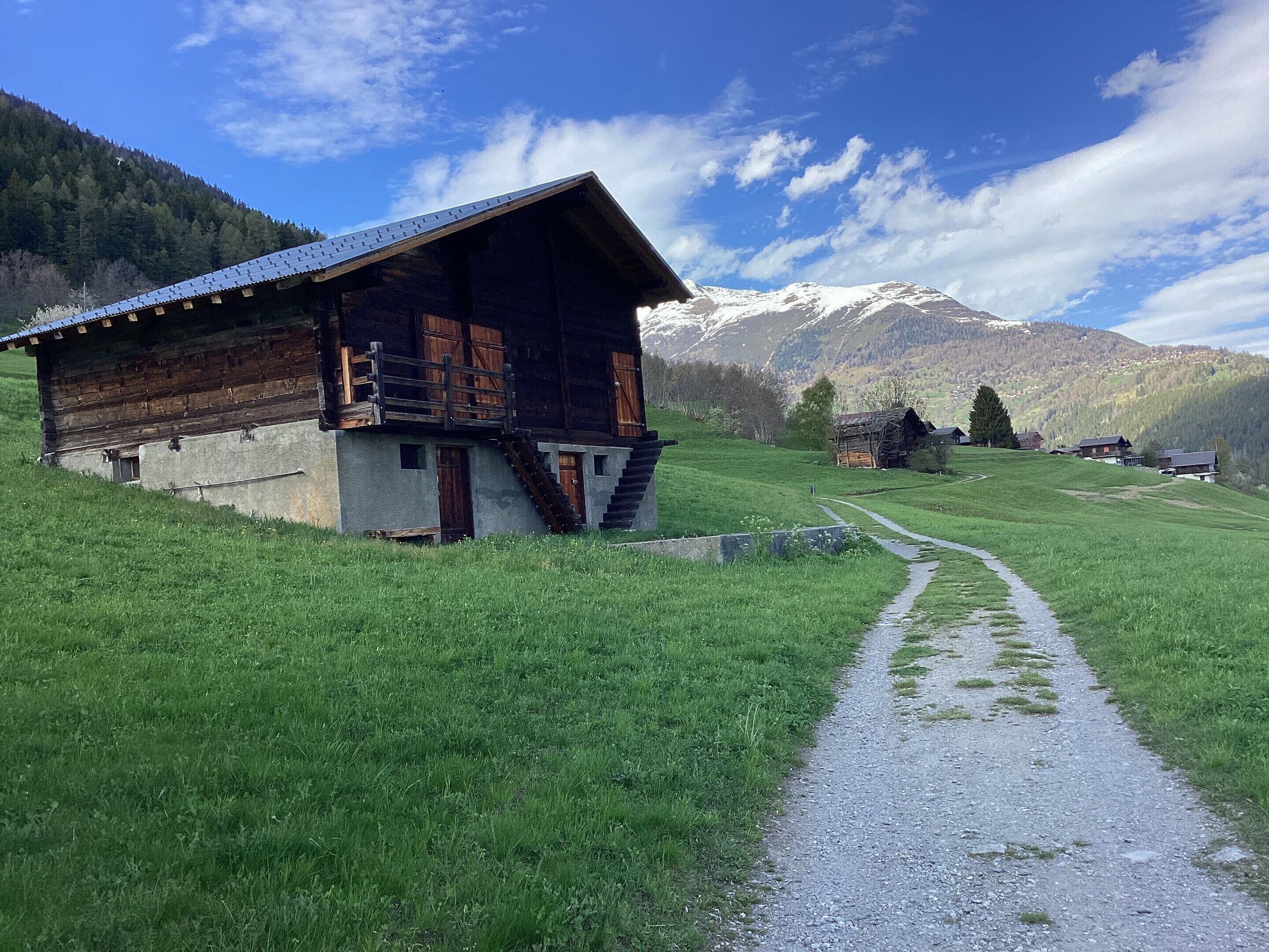 A wooden chalet with a sloped roof, a stone foundation, and a gravel path leading to it.