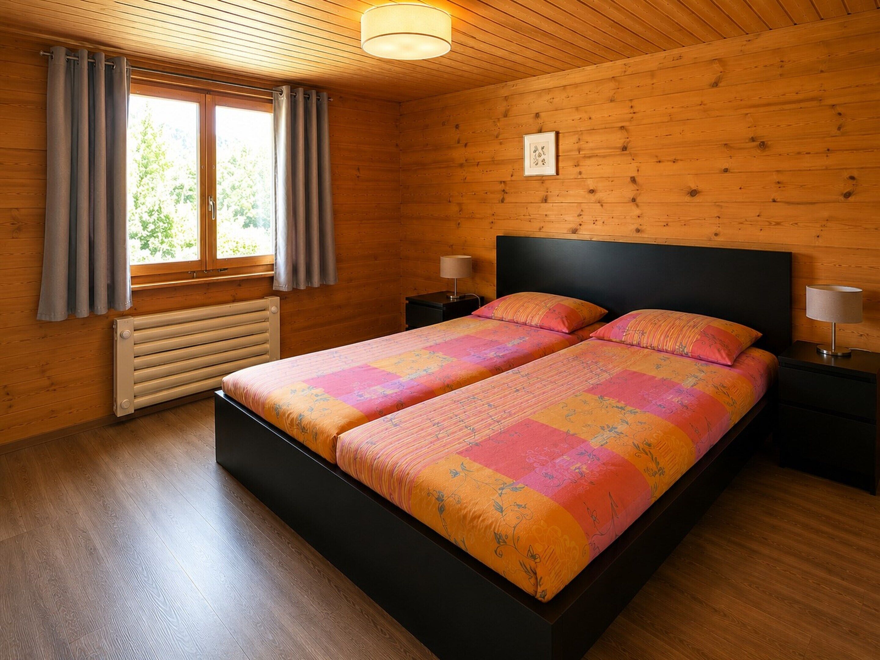 A wooden-paneled bedroom with a bed, two bedside tables, a window with curtains, and a radiator.