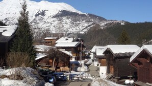 Un village enneigé, avec des bâtiments en bois, un ciel dégagé et une montagne en arrière-plan.