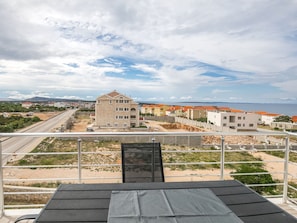 A balcony with a view of a coastal area, featuring a building with a stone facade and a modern structure with orange roofs. - Apartment in Novalja Near Zrce Beach (Novalja)