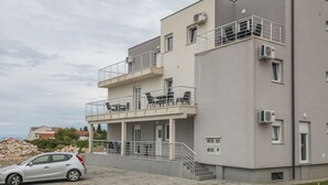 A modern two-story building with balconies, a car parked in front, and a stone wall in the background. - Apartment in Novalja Near Zrce Beach (Novalja)