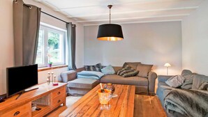 A modern living room with a wooden coffee table, a sofa, a TV, and a window with curtains. - Scenic Stay in Xhoffraix (Malmedy)