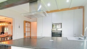A modern kitchen with a large island, stainless steel appliances, and wooden stools. - Scenic Stay in Xhoffraix (Malmedy)