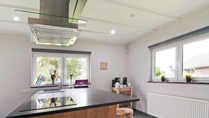 A modern kitchen with a central island, a built-in stove, and a window with a view of trees. - Scenic Stay in Xhoffraix (Malmedy)