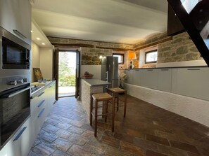 A modern kitchen with a stone accent wall, a built-in oven, and a large island with stools. - Belvilla by OYO Fattoria 19 (Amandola)